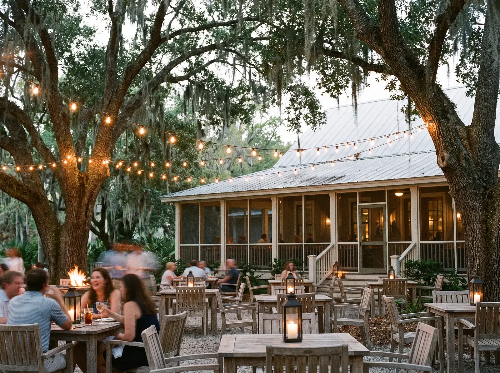 Outdoor lowcountry-style restaurant and bar terrace at dusk under string lights